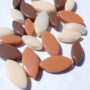 May include: A collection of oval-shaped beads in various shades of brown, tan, and cream. The beads have a glossy finish and are scattered across a white surface. These beads could be used for jewelry making or other craft projects.