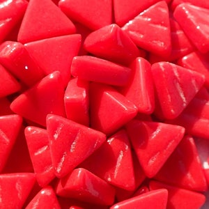 May include: A close-up of a pile of small, red, triangular glass tiles. The tiles have a textured surface and are arranged in a random pattern.
