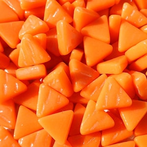 May include: A close-up of a pile of small, orange, triangular glass tiles. The tiles are smooth and shiny, and they have a slight iridescent sheen.