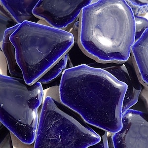 May include: A collection of blue ceramic tile pieces with irregular edges. The tiles have a glossy finish and are arranged in a random pattern.