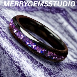 Op de afbeelding: Een donkere houten ring met een band van sprankelende paarse en blauwe edelstenen. De ring heeft een glanzend zwart interieur en de tekst "MERRYGEMSSTUDIO" in het wit.