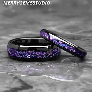 May include: Two black rings with a band of purple and blue crushed stone. The rings are set against a gray background. The text "MERRYGEMSSTUDIO" is at the top of the image.
