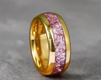 May include: A gold-colored ring with a band of pink, crushed stone. The ring has a polished, smooth finish and a wide band. The brand name "MERRYGEMSSTUDIO" is visible at the top of the image. This ring is a piece of jewelry.
