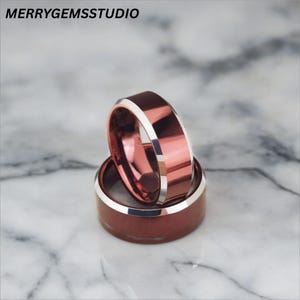 Peut inclure: Deux bagues empilées avec un design à large bande. Les bagues ont un intérieur brun rougeâtre et un bord argenté. Les bagues sont posées sur un fond en marbre. Le texte "MERRYGEMSSTUDIO" est dans le coin supérieur gauche.