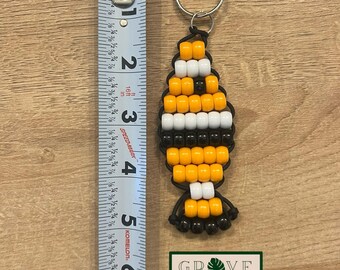 May include: A handmade beaded keychain in a fish shape, featuring orange, white, and black beads. The keychain is approximately 3 inches long. The design includes a metal keyring and the text "GROVE HAND MADE" on a green and white label.