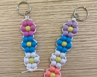 May include: Two handmade beaded flower keychains. Each keychain features a flower design with colorful beads in shades of pink, blue, white, and yellow. The keychains are attached to silver key rings. The text "GROVE HAND MADE" is in a green rectangle.