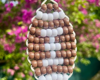 May include: A football-shaped keychain crafted from brown and white plastic pony beads strung on white cord. The design features a central vertical white stripe with horizontal white laces, surrounded by brown beads, attached to a silver metal ring.