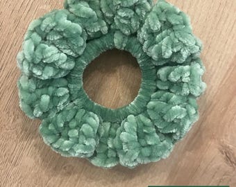 May include: A sage green velvet scrunchie with a soft, textured appearance. The scrunchie is circular, with a visible elastic band in the center. The scrunchie is handmade, as indicated by the text "GROVE HAND MADE" in a small rectangular logo.