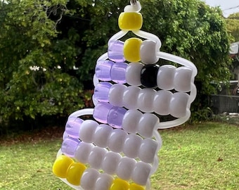 May include: A handmade keychain featuring a colorful design of yellow, white, black, and purple beads. The keychain is attached to a silver metal ring. The bottom of the image shows a green and white sign that reads "GROVE HAND MADE".
