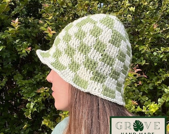 May include: A handmade crochet bucket hat in a green and white checkerboard pattern. The hat has a small brim and is shown from the side. The hat is labeled "GROVE HAND MADE" in a green and white rectangular logo.