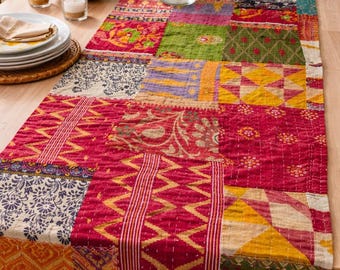 Puede incluir: Un camino de mesa de patchwork colorido con una variedad de patrones y colores, incluyendo rojo, amarillo, verde y azul. El camino de mesa está sobre una mesa de madera, con un jarrón de flores encima.
