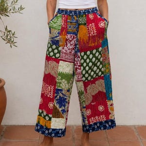 Puede incluir: Pantalones patchwork de pernera ancha. Presentan una variedad de parches de tela coloridos en rojo, verde, azul y amarillo. La cintura es azul liso y los pantalones tienen bolsillos. La modelo lleva un top blanco. Largo aproximado: 90 cm.