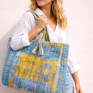 Könnte beinhalten: Eine große Tragetasche mit einem Patchwork-Design in Blau- und Gelbtönen. Die Tasche hat eine rechteckige Form mit einem quadratischen gelben Feld in der Mitte. Die Tasche hat zwei Griffe und eine Quaste. Die Tasche ist aus gewebtem Stoff.