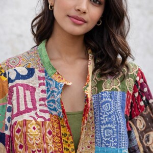 May include: A colorful patchwork jacket with a green collar and a variety of patterned fabric squares. The jacket is open, revealing a green top underneath. The jacket's design includes shades of blue, yellow, red, and white.