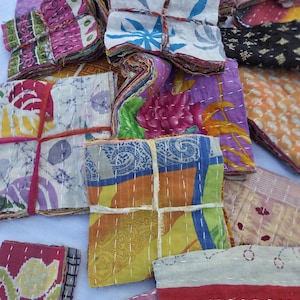 May include: A collection of colorful, patterned fabric bundles tied with string. The fabrics feature floral and geometric designs in shades of pink, purple, yellow, blue, and orange. The bundles are stacked together, showcasing the variety of patterns.