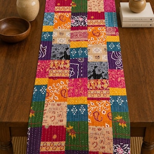 May include: A rectangular table runner featuring a vibrant patchwork design composed of various fabric squares. The textile displays a multitude of colours including magenta, orange, yellow, blue, green, and purple, with intricate floral and geometric patterns.