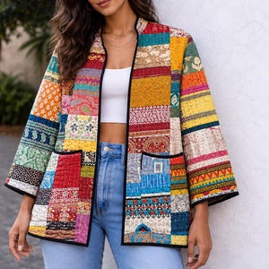 May include: A long-sleeved jacket featuring a vibrant patchwork design with various colorful patterns including floral, geometric, and paisley motifs. The jacket has a black trim along the open front and two front pockets, with visible kantha stitching.