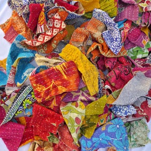 May include: A pile of colorful, patchwork fabric scraps in various sizes and shapes. The fabrics feature a variety of patterns, including floral, geometric, and abstract designs. The colors include red, blue, yellow, orange, and green. The pieces are stitched together with white thread.