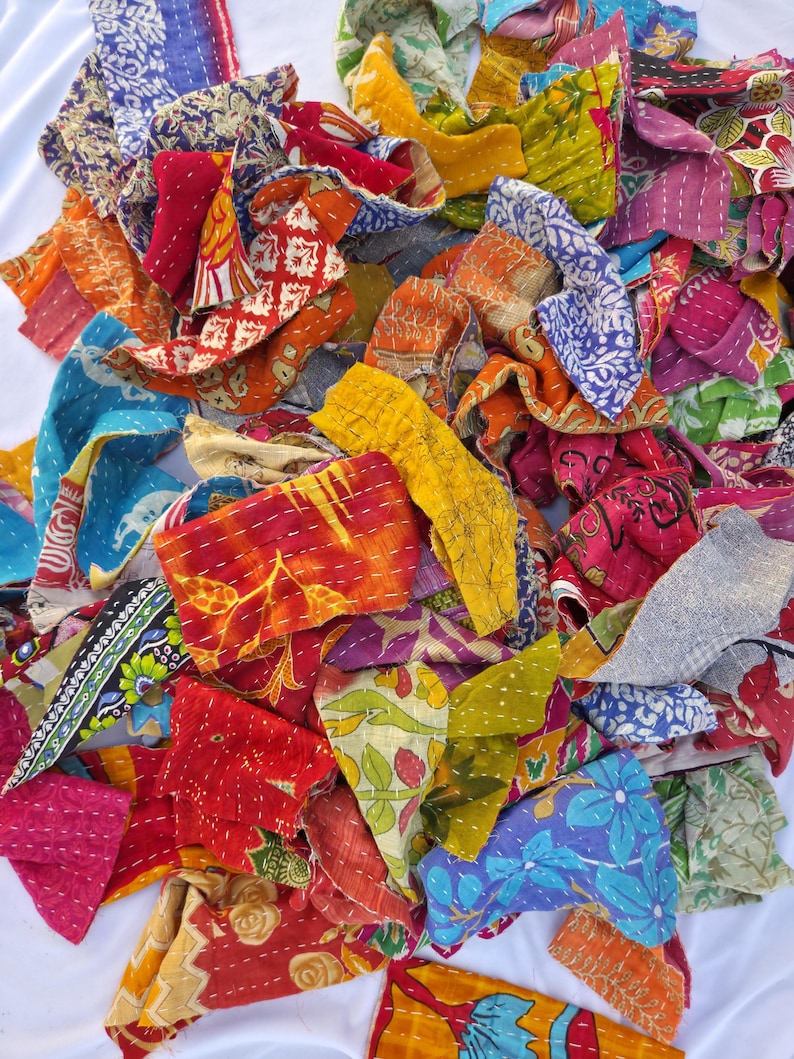 May include: A pile of colorful, patchwork fabric scraps in various sizes and shapes. The fabrics feature a variety of patterns, including floral, geometric, and abstract designs. The colors include red, blue, yellow, orange, and green. The pieces are stitched together with white thread.