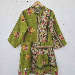 Könnte beinhalten: Eine grüne Jacke mit langen Ärmeln und einem Blumenmuster in Rot, Gelb und Weiß. Die Jacke ist aus gestepptem Stoff gefertigt und hat eine Knopfleiste vorne. Die Jacke hängt an einem Holzbügel.