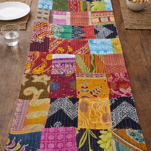 Puede incluir: Un camino de mesa de patchwork colorido con una variedad de cuadrados de tela estampada. El camino de mesa presenta una mezcla de colores vibrantes, incluyendo rojo, amarillo, azul y verde. El camino de mesa est&aacute; colocado sobre una mesa de madera.
