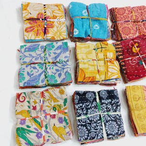 May include: A collection of colorful fabric bundles, each tied with string. The fabrics display various floral and geometric patterns in shades of blue, yellow, red, and white. The bundles are neatly stacked, showcasing a variety of designs.