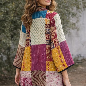 May include: A quilted jacket featuring a patchwork design of various floral and geometric patterns in shades of maroon, mustard yellow, cream, and blue. The garment has three-quarter length sleeves, a straight hem, and black trim along the edges.