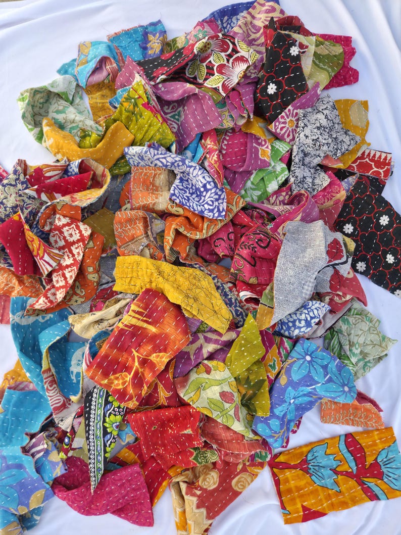May include: A pile of colorful fabric scraps with various floral and geometric patterns. The scraps are in shades of red, orange, yellow, green, blue, and purple. The fabric appears to be hand-stitched, with visible thread lines.