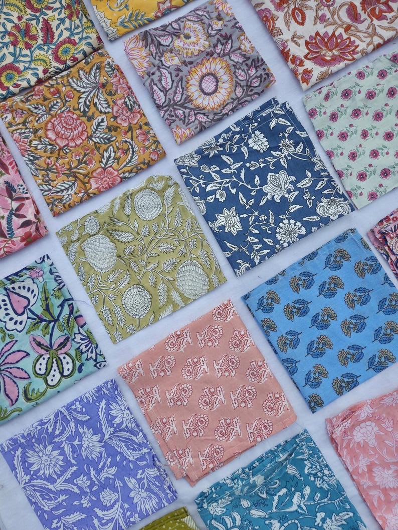 May include: An assortment of colorful, square fabric pieces with floral and botanical patterns. The fabrics feature a variety of colors, including yellow, blue, pink, and green, with intricate designs. The arrangement showcases the diverse patterns and colors.