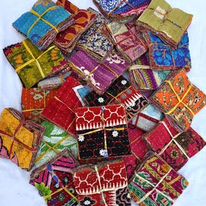 May include: A collection of colorful, square fabric bundles tied with yellow or light brown twine. The bundles display a variety of patterns and colors, including red, blue, green, and purple. The fabrics appear to be quilted or stitched.