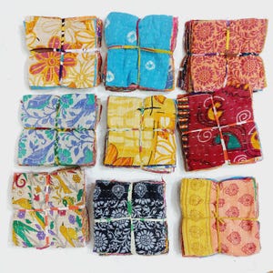 May include: Nine bundles of colorful fabric squares, each tied with twine. The fabrics feature floral and geometric patterns in various colors, including blue, yellow, red, and orange. The bundles are arranged in a grid.