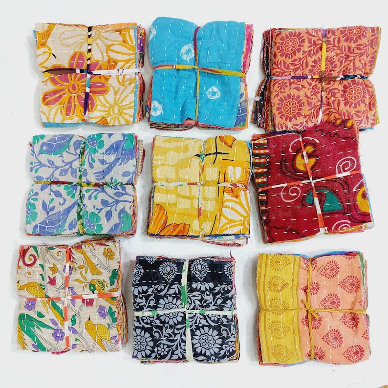 May include: Nine bundles of colorful fabric squares, each tied with twine. The fabrics feature floral and geometric patterns in various colors, including blue, yellow, red, and orange. The bundles are arranged in a grid.