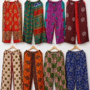 May include: Eight pairs of wide-leg trousers with elastic waistbands, each featuring distinct colorful patterns including floral, geometric, and paisley prints in shades of red, green, purple, blue, orange, and cream, all hanging on wooden hangers.