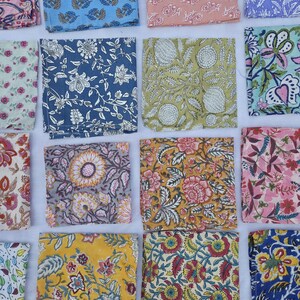 May include: A collection of colorful, square fabric napkins with floral patterns. The napkins feature various designs in shades of blue, pink, yellow, and green. The patterns include stylized flowers and leaves, creating a vibrant and decorative display.