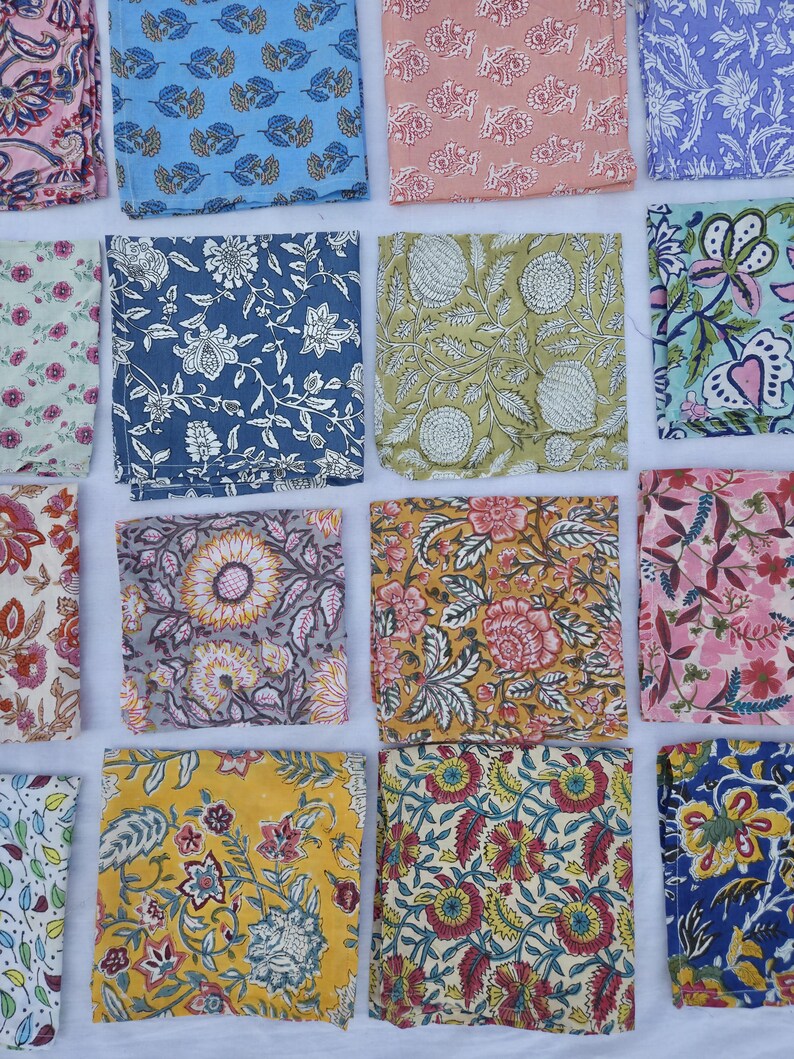 May include: A collection of colorful, square fabric napkins with floral patterns. The napkins feature various designs in shades of blue, pink, yellow, and green. The patterns include stylized flowers and leaves, creating a vibrant and decorative display.