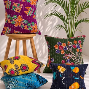 May include: A collection of decorative throw pillows with colorful, embroidered designs. The pillows feature various patterns, including floral and geometric motifs, in shades of purple, green, yellow, and blue. The pillows are square-shaped and appear to be made of fabric.