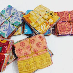 May include: Stacks of colorful, patterned fabric squares tied with twine. The fabrics feature floral and geometric designs in shades of blue, yellow, orange, and red. The squares are likely part of a textile craft project.