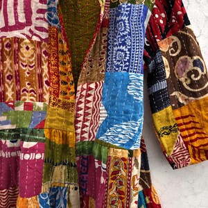 May include: A patchwork jacket with a variety of colorful fabric patterns. The jacket features a mix of floral, geometric, and abstract designs in shades of red, blue, green, yellow, and pink. The jacket has long sleeves and a collar.