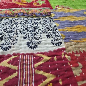 Puede incluir: Primer plano de un textil patchwork con varios patrones y colores. El edred&oacute;n presenta secciones de telas rojas, verdes, moradas y crema. Los dise&ntilde;os incluyen estampados florales, formas geom&eacute;tricas y detalles cosidos a mano. La est&eacute;tica general es r&uacute;stica y artesanal.
