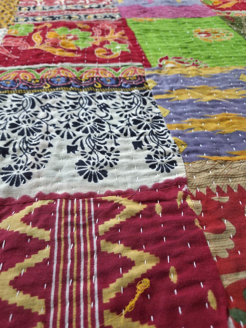Puede incluir: Primer plano de un textil patchwork con varios patrones y colores. El edred&oacute;n presenta secciones de telas rojas, verdes, moradas y crema. Los dise&ntilde;os incluyen estampados florales, formas geom&eacute;tricas y detalles cosidos a mano. La est&eacute;tica general es r&uacute;stica y artesanal.