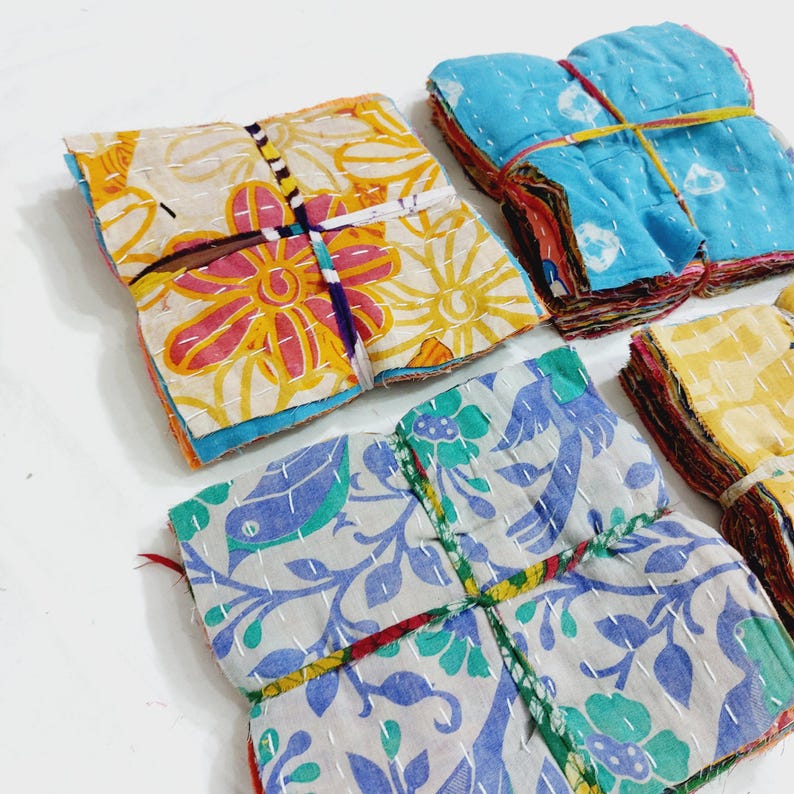 May include: Stacks of colorful, patterned fabric squares, likely coasters or small decorative items. The fabrics feature floral and abstract designs in shades of yellow, blue, and white, with visible stitching and bound with twine.