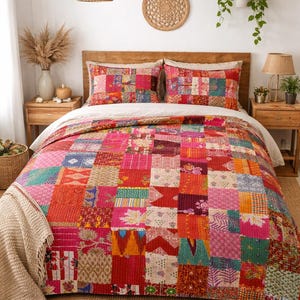 Könnte beinhalten: Ein farbenfrohes Patchwork-Quilt und passendes Kissen-Set auf einem Bett. Der Quilt besteht aus verschiedenen Stoffquadraten in Rot-, Rosa-, Orange- und Grüntönen. Das Bett ist mit einem weißen Laken und einem hölzernen Kopfteil ausgestattet.
