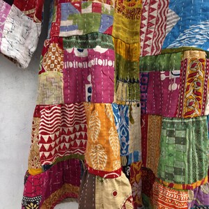 May include: A patchwork garment featuring a vibrant mix of colors and patterns. The design incorporates various fabric pieces stitched together, showcasing a range of textures and hues, including red, yellow, blue, and pink. The garment has a layered appearance with visible seams.