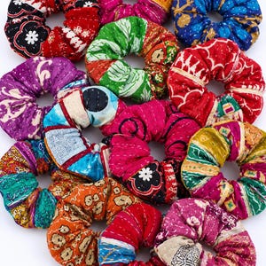 May include: A collection of twelve fabric hair scrunchies featuring various colorful patterns, including floral, geometric, and abstract designs. Each scrunchie is constructed from quilted fabric with visible stitching, showcasing a mix of red, blue, green, purple, orange, and yellow hues.