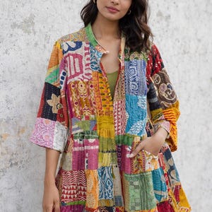 Könnte beinhalten: Bunte Patchwork-Jacke mit Stehkragen und Dreiviertelärmeln. Die Jacke besteht aus verschiedenen gemusterten Stoffen in Rot-, Gelb-, Blau- und Grüntönen. Sie hat Taschen und ein gestuftes Design.