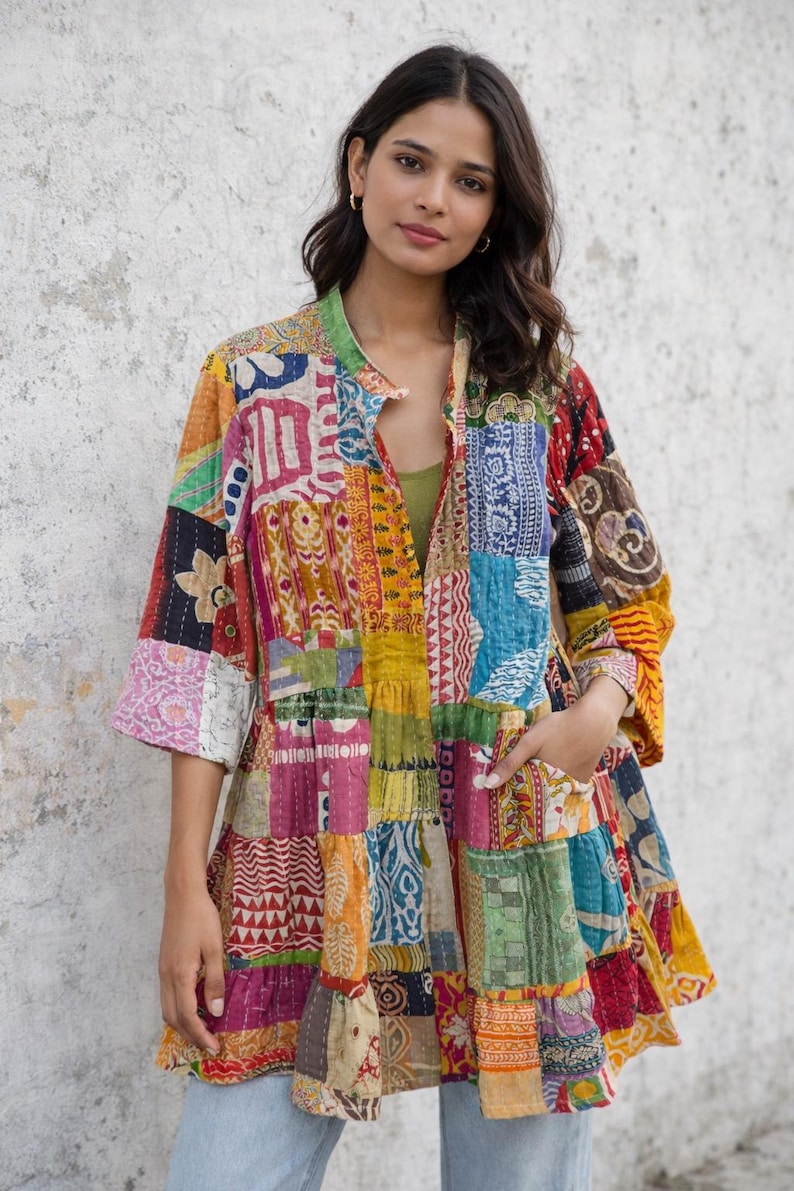 May include: A colorful patchwork jacket with a mandarin collar and three-quarter sleeves. The jacket features a variety of patterned fabrics in shades of red, yellow, blue, and green. The jacket has pockets and a tiered design.
