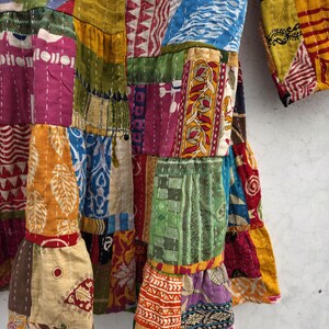 May include: A patchwork garment with a variety of colorful fabric squares. The garment features a mix of patterns, including floral, geometric, and abstract designs. The sleeves and hem have a ruffled edge. The stitching is visible throughout the garment.