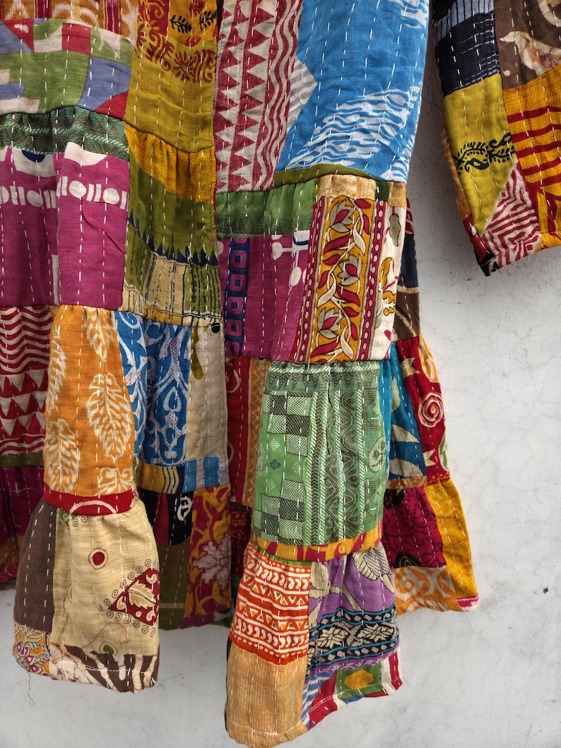May include: A patchwork garment with a variety of colorful fabric squares. The garment features a mix of patterns, including floral, geometric, and abstract designs. The sleeves and hem have a ruffled edge. The stitching is visible throughout the garment.