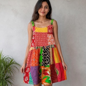 Könnte beinhalten: Ein Patchwork-Minikleid mit einer lebendigen Mischung aus Farben und Mustern. Das Kleid hat einen quadratischen Ausschnitt, breite Träger und eine geraffte Taille. Der Stoff scheint eine Mischung aus verschiedenen Textilien zu sein, was ein einzigartiges Design ergibt.