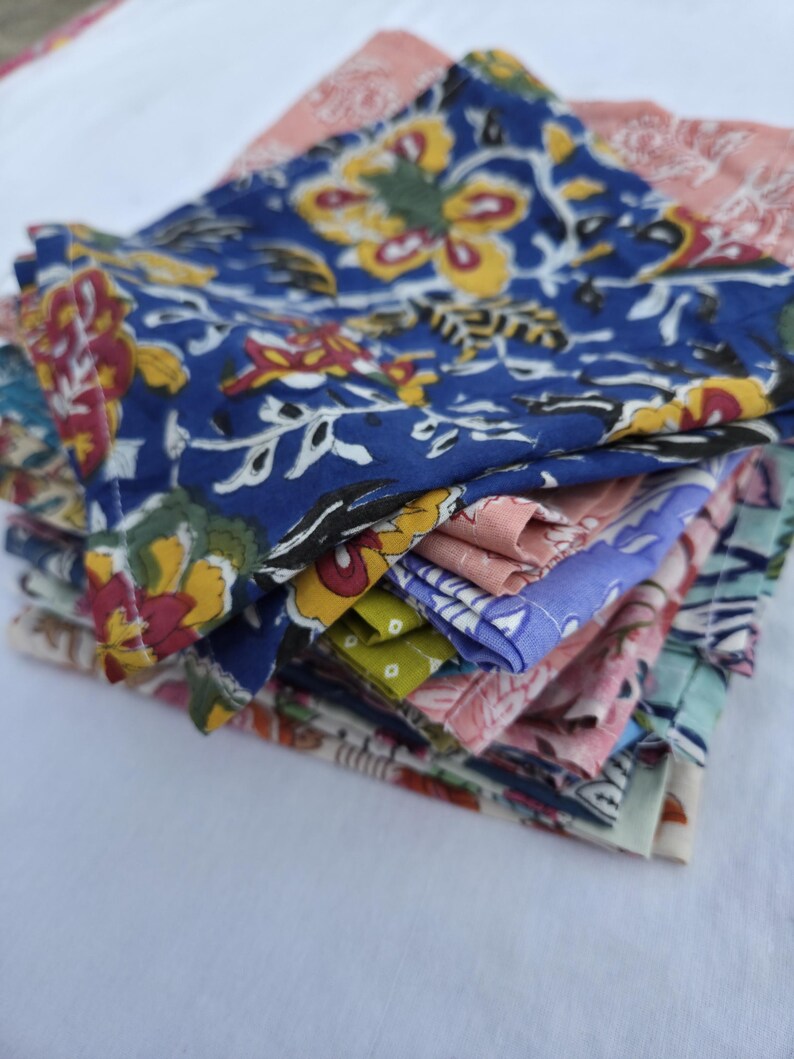 May include: A stack of colorful fabric napkins with floral patterns. The napkins feature a variety of colors, including blue, pink, yellow, and green. The floral designs include large flowers and intricate details.
